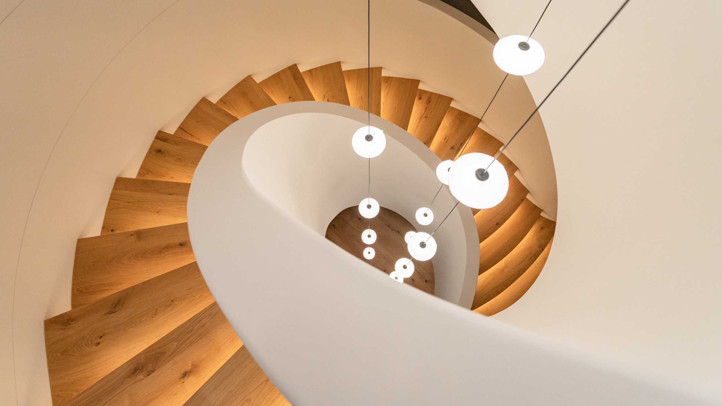 Completed curved staircase with wooden steps and smooth white balustrade.